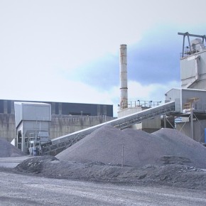 A photograph of quarry with equipment and warehouse in the background and heaps of sand in the foreground