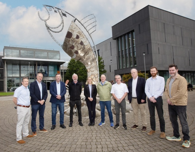 A group of URL people standing infront of a fish sculpture