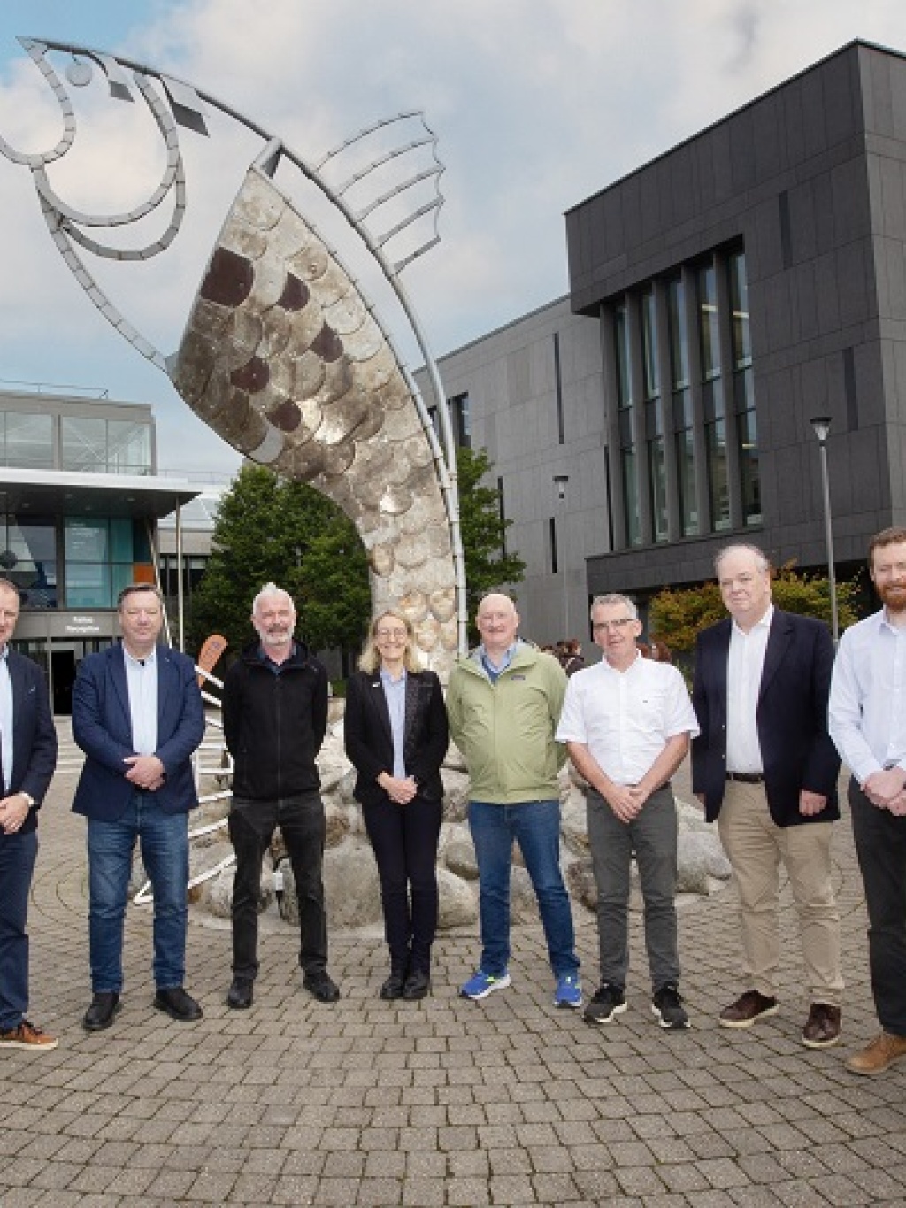 A group of URL people standing infront of a fish sculpture