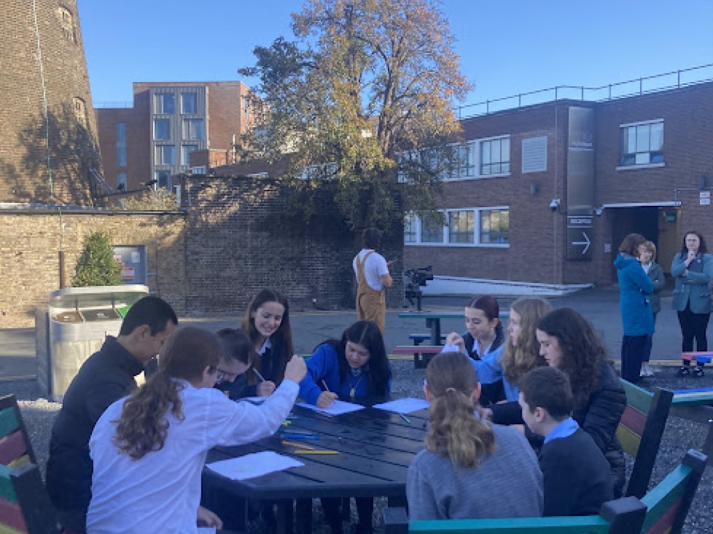 Students drawing and chatting at a table in a school yard